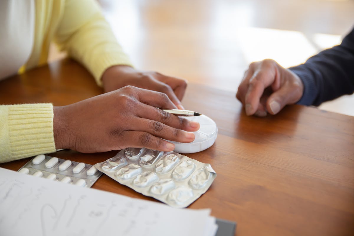 Person discussing tablet medication at a table with a pen and blister pack